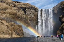 A group of people standing at the base of a waterfall with a rainbow. over them