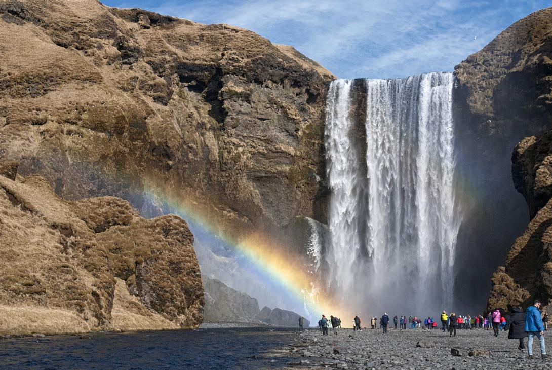 A group of people standing at the base of a waterfall with a rainbow. over them